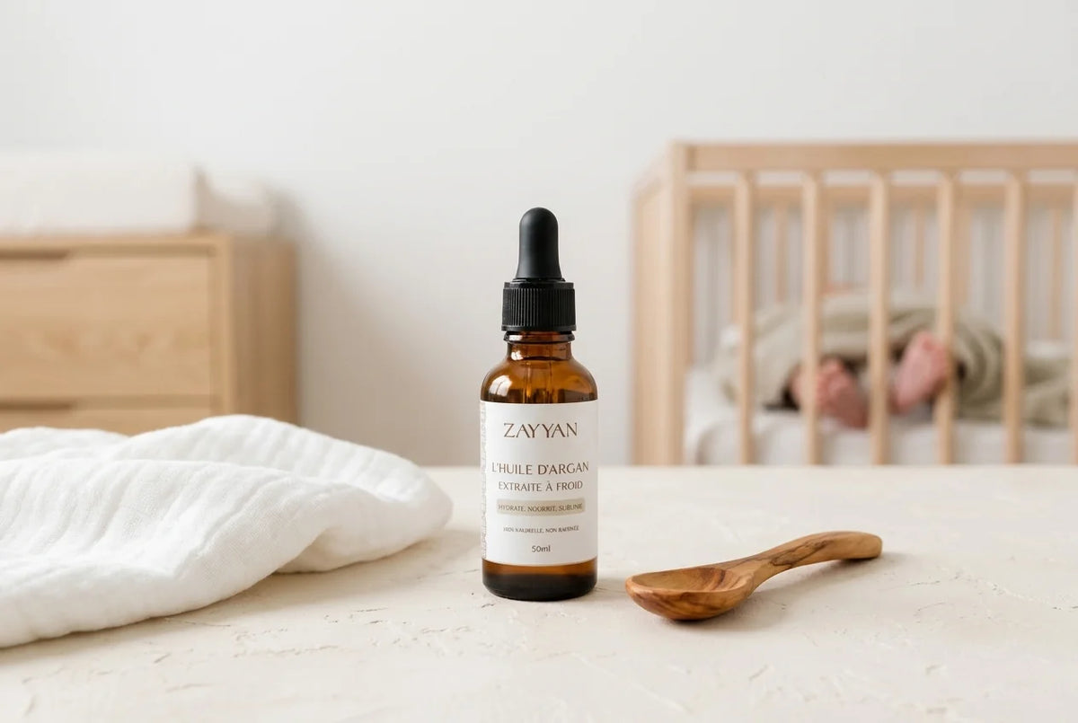 Flacon d'huile d'argan Zayyan posé près d'un lange en coton et d'une cuillère en bois d'olivier, dans une chambre de bébé