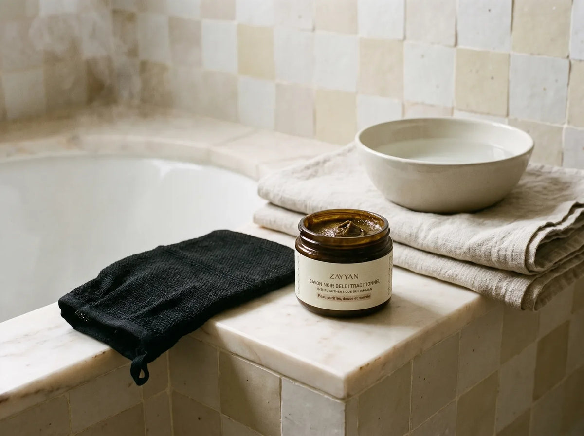 Savon noir et gant kessa Zayyan posés côte à côte sur une tablette de hammam en marbre clair