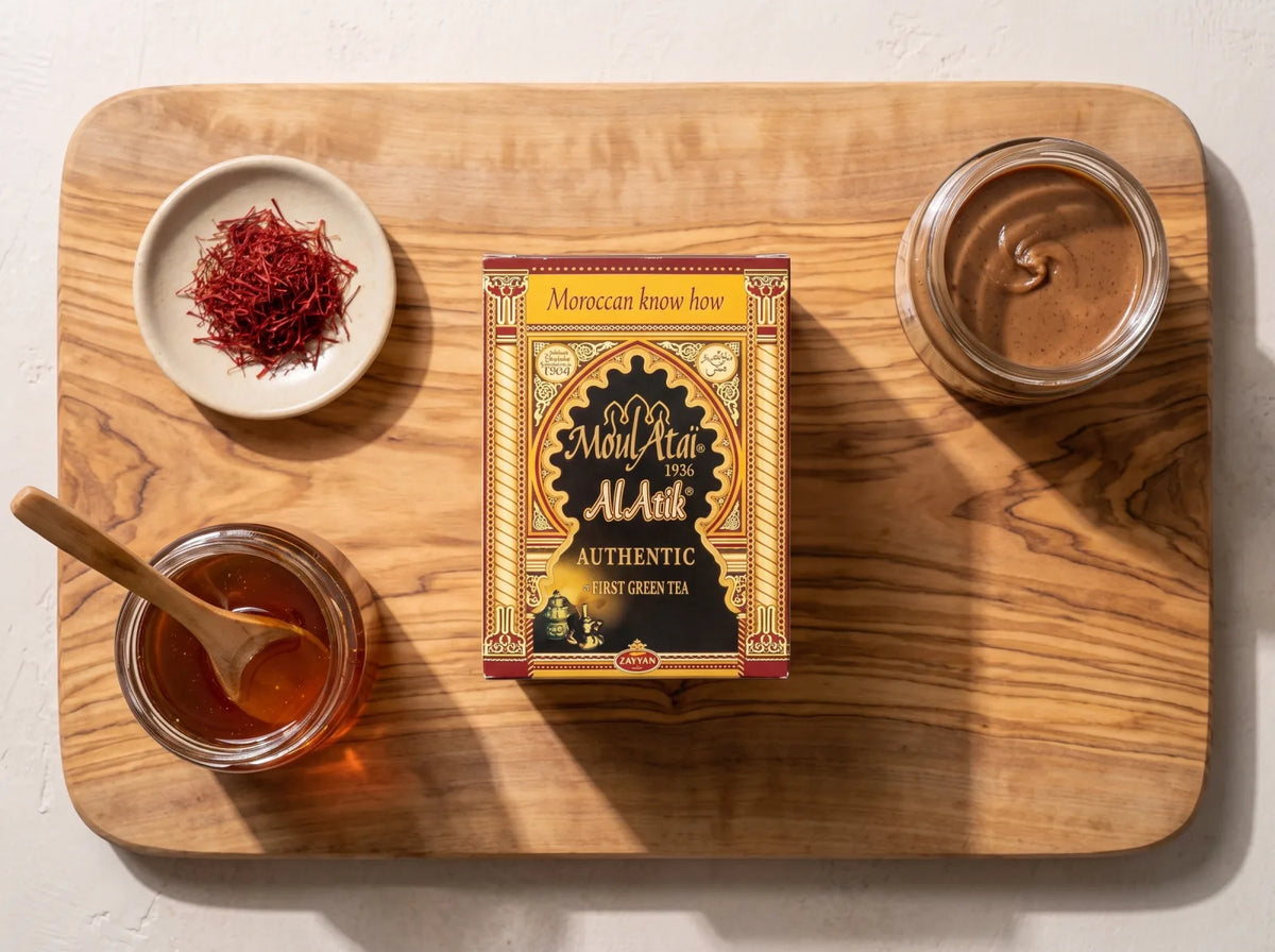Épicerie fine marocaine à plat sur une planche en bois : thé vert El Atik, safran, miel de thym et amlou