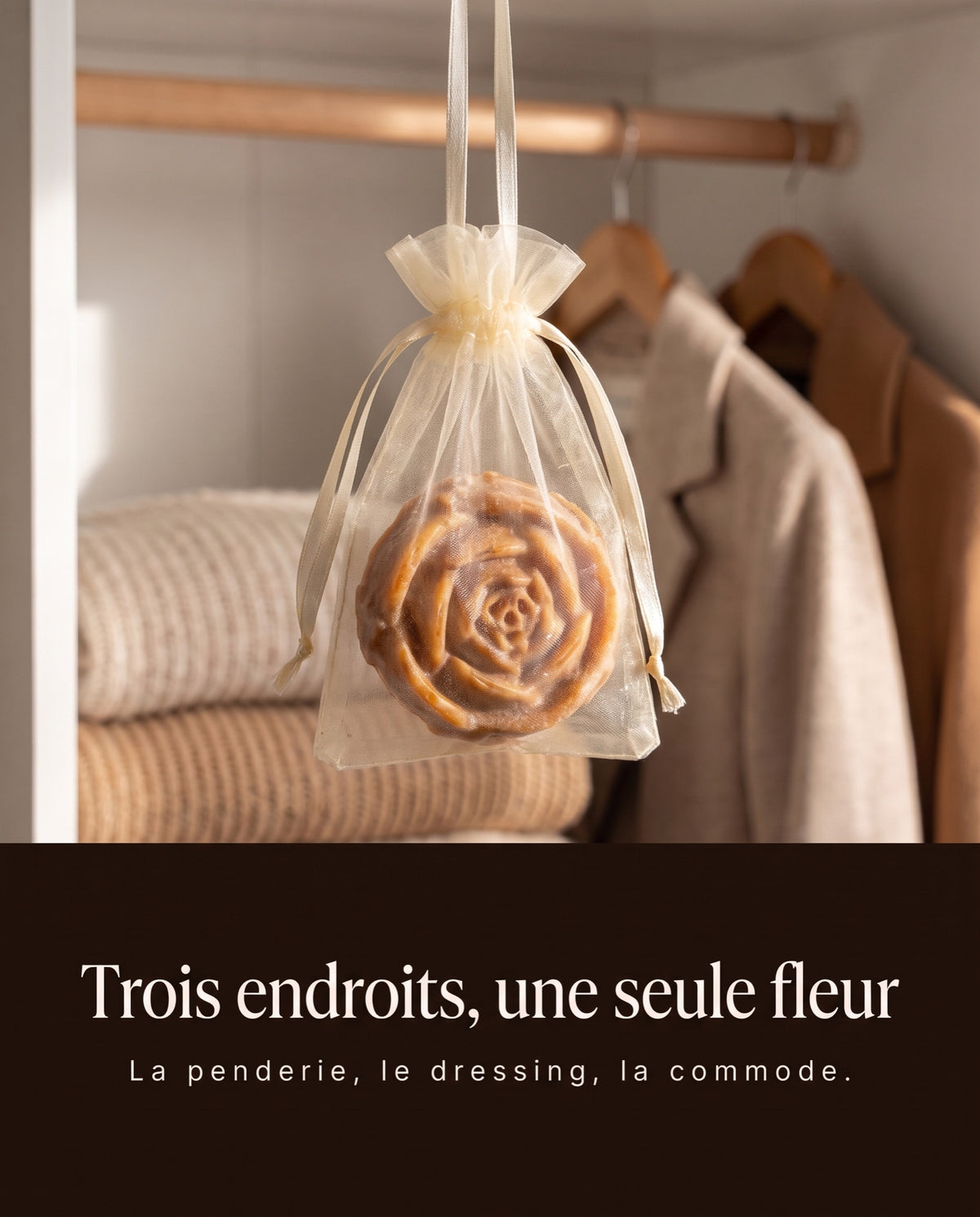 Fleur d'Ambre dans son sachet en organza, suspendue dans une penderie entre les pulls et les chemises
